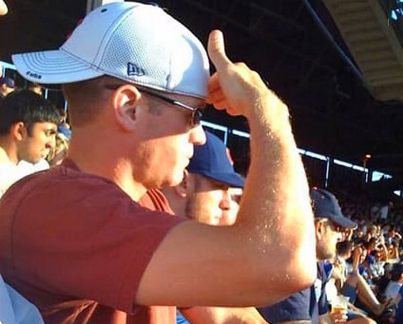 Un hombre se protege del sol con la mano a la vez que viste una gorra con la visera hacia detrás.